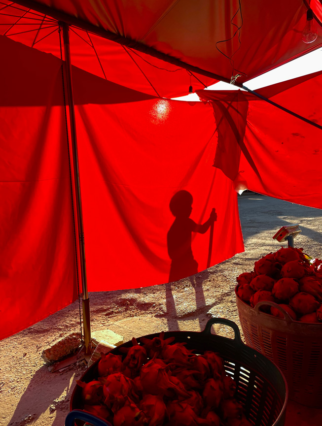 Proyección de la sombra de un niño que juega sobre una lona roja colocada para tapar el sol.