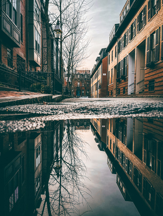 Un gran charco de agua en la calle refleja los alrededores y el cielo.