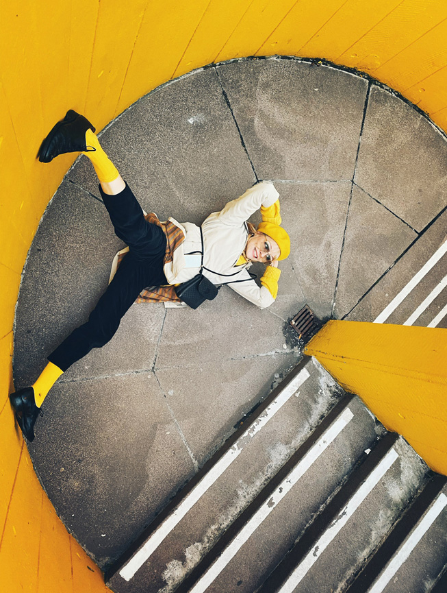 Una persona posa en el rellano de una escalera con paredes amarillas.